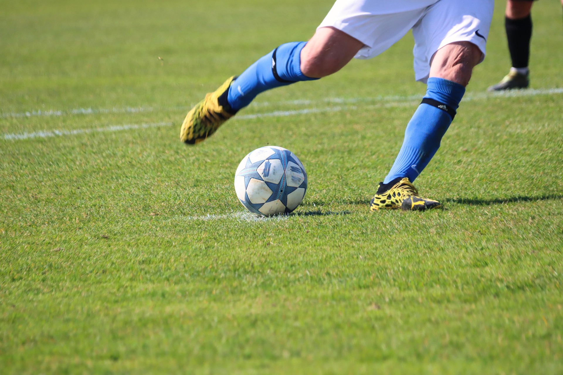 An image of a players legs kicking a soccer ball on a pitch